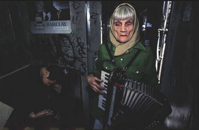 An old lady is seen playing accordion to earn some buck in the train. She looks totally desolated while playing the instrument